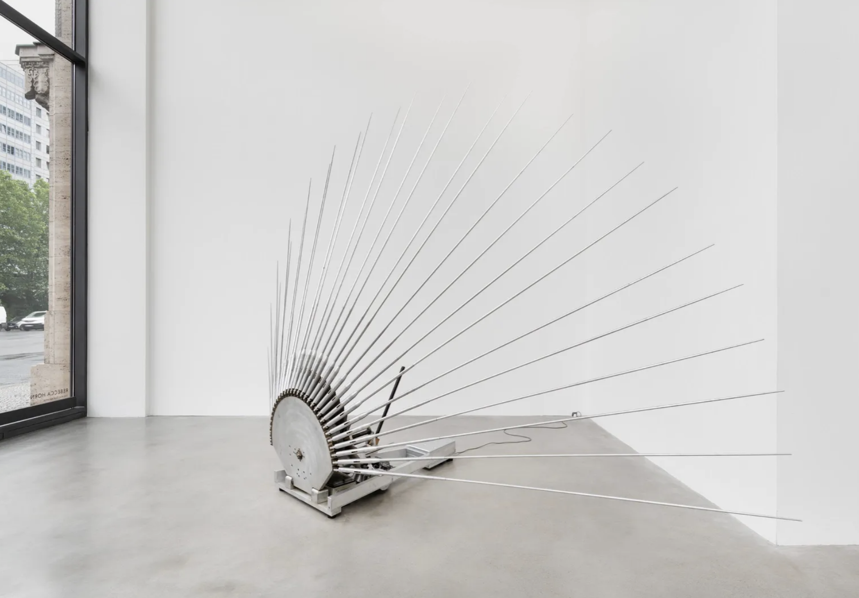 Halbkreisförmige Metallskulptur mit fächerförmig ausstrahlenden dünnen Stangen in weißer Galerie